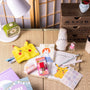 The Inku Stationery Crate by Japan Crate features kawaii items like Pikachu and Miffy notebooks and accessories, displayed on a tatami mat with a green clock, lamp, and wooden drawers. thumbnail 5