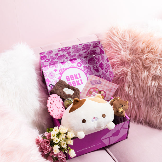 A Doki Doki Kawaii Crate by Japan Crate, filled with kawaii Japanese plushies, flowers, and stationery, sits on a light pink sofa with fluffy pillows.