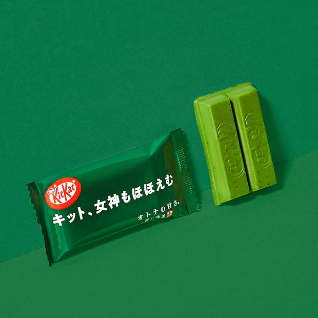 Japanese Kit Kat: Rich Green Tea bar by Nestle Japan partially unwrapped with a piece broken off, on a matching green background.