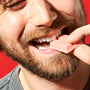 A close-up of a smiling man with a beard eating a piece of bittersweet Nestle Japan Japanese Kit Kat: Strawberry Otona no Amasa against a red background. thumbnail 3