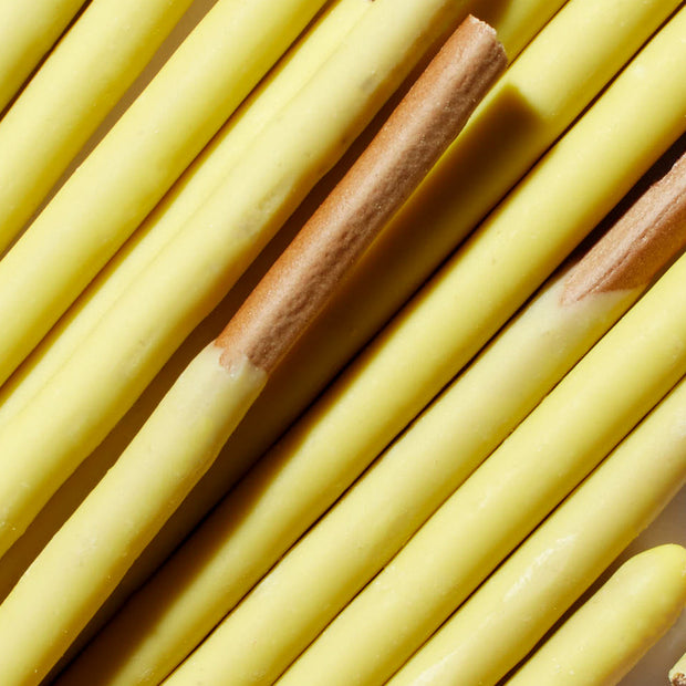 Close-up of yellow, chocolate-covered biscuit sticks arranged in parallel lines, reminiscent of a classic Bokksu Market Pocky Variety Pack (12-Pack).