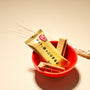 A Nestle Japan Japanese Kit Kat: Whole Wheat Cookie in a red bowl with a golden wrapper, displayed next to dried wheat stalks on a beige surface, appealing to health-conscious snackers. thumbnail 3