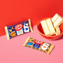 Two Nestle Japan Milk Tea Kit Kat flavor bars beside a bowl of white chocolate pieces on a red surface, contrasting with a pink background. thumbnail 2