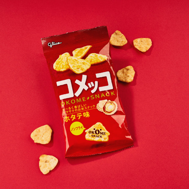 Glico Komeko Scallop snacks, featuring irregularly shaped, crispy scallop-flavored chips scattered around their bright red packaging, emphasizing their savory taste and bite-size appeal. Brand: Bokksu Market; Product: Glico Komeko: Scallop.