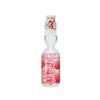 The image features a Hata Ramune Soda: Lychee (6.76 oz) bottle. The packaging is predominantly white and pink, with illustrations of lychee fruit and Japanese text. This carbonated Japanese soda is known for its marble-sealed glass bottle, which adds a fun and interactive twist to drinking. Brand: Bokksu Market; Product: Hata Ramune Soda: Lychee (6.76 oz).