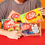 A person holding the Nestle Japan Japanese Kit Kat 6 Flavor Variety Pack (6-pack) including milk tea and other assortments, against a red background. thumbnail 2