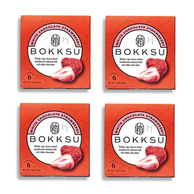 Four boxes of Bokksu White Strawberry 6-Piece Box (4-Pack), each containing six pieces of whole, ripe, freeze-dried strawberries covered in white chocolate. This artisanal Japanese snack from Bokksu comes in red packaging with an image of a strawberry.