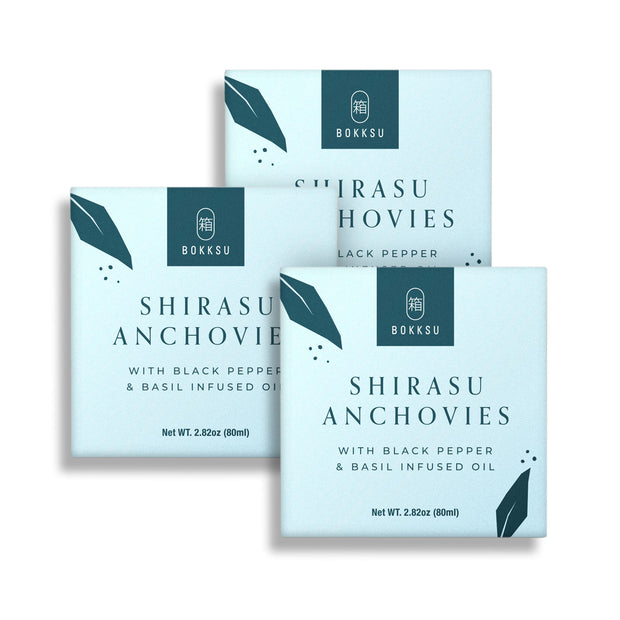 Three boxes of Bokksu Tinned Shirasu Anchovies with Black Pepper and Basil-Infused Oil (3-Pack), each with a net weight of 2.82 oz (80 ml), are arranged against a white background. Perfect for adding to umami spaghetti dishes or enjoying as premium canned fish.