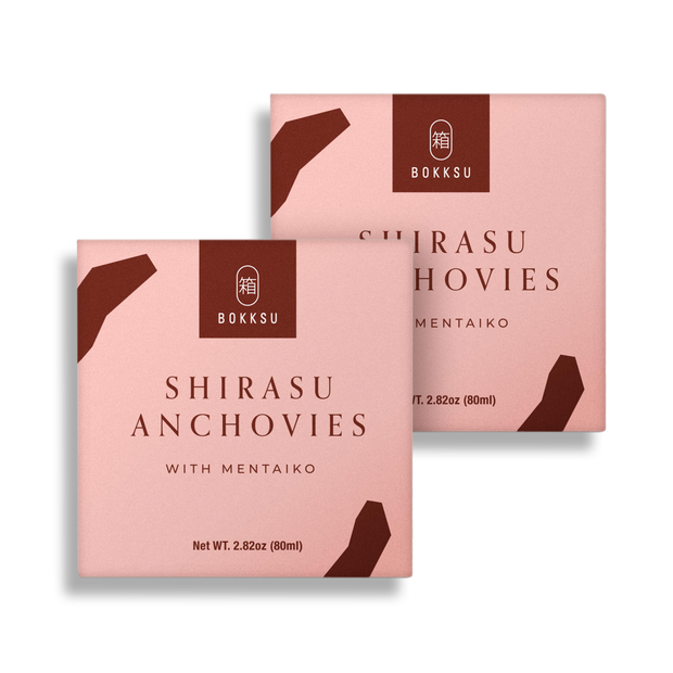 Two pink boxes of Bokksu's Tinned Shirasu Anchovies with Cod Roe (2-Pack), a prized Japanese delicacy, each having a net weight of 2.82 oz (80 ml) and blending shirasu anchovies and cod roe flavors in every bite.