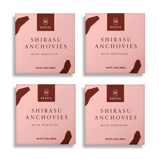 Four packages of Bokksu Tinned Shirasu Anchovies with Cod Roe (4-Pack), a delectable Japanese delicacy featuring cod roe, each with a net weight of 2.82 ounces (80g), are displayed. The packaging is pink and brown with text and a logo.