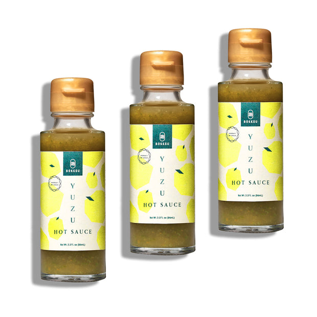 A 3-pack of Bokksu Yuzu Hot Sauce by Bokksu features spicy and tangy bottles with yellow caps and green labels decorated with lemon graphics and text.