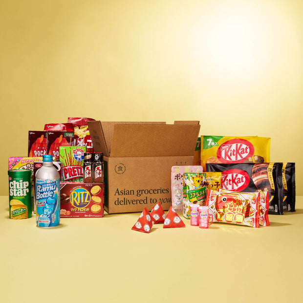 The Discovery Pack by Bokksu Market features Asian snacks, instant ramen, and drinks arranged around an open box labeled "Asian groceries delivered to you" on a yellow background.