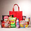 The Snack Attack Lucky Bag from Bokksu Market features a reusable tote behind an assortment of Japanese snacks like KitKat, Lay’s chips, Pocky, Ramune soda, and various colorful candies and cookies.