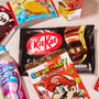 The Snack Attack Lucky Bag by Bokksu Market is filled with Japanese snacks like a black KitKat bag, Super Mario chocolate, Ramune grape soda, and assorted colorful treats displayed on a light surface. thumbnail 5