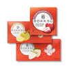 Three Bokksu Market Japanese Candy Bites Trio Delight boxes are stacked, highlighting white strawberry and sour yuzu snacks, with fruit images displayed on the packaging.