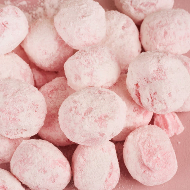 A close-up of Bokksu Market’s Japanese Candy Bites Duo: White Strawberry & Sour Yuzu—round, pink powdered confections—arranged closely together on a pink surface.