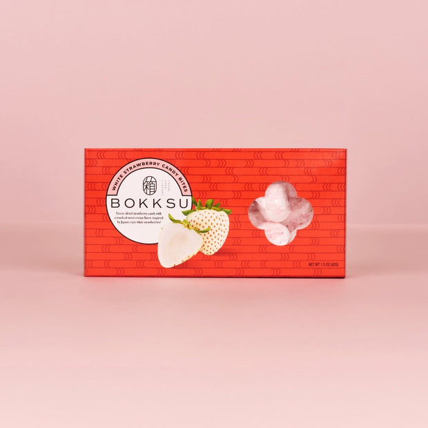 A red box of Bokksu Market White Strawberry Japanese Candy Bites (3-Pack) is shown against a pink background, featuring images of freeze-dried bites and juicy white strawberries covered in creamy white chocolate on the front.