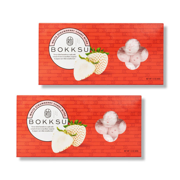 Two red Bokksu Market boxes labeled "White Strawberry Japanese Candy Bites (2-Pack)" feature images of white strawberries and a window displaying the round treats—a delicious white chocolate-infused, freeze-dried candy.