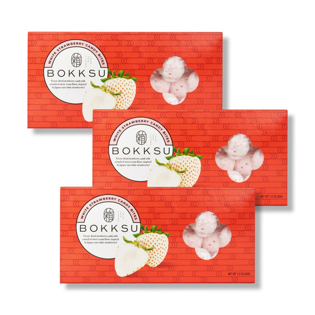 Three boxes of Bokksu Market’s White Strawberry Japanese Candy Bites (3-Pack) are stacked, each showing white strawberries and candy pieces through a clear window on the packaging.