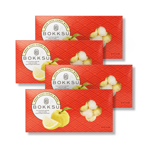 Four Sour Yuzu Japanese Candy Bites (4-Pack) from Bokksu Market are displayed overlapping on a white background, with orange packaging showcasing Japanese citrus designs and enticing candy pieces.