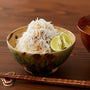 A bowl filled with white rice topped with Bokksu Tinned Shirasu Anchovies with Yuzu Pepper (3-Pack), garnished with lime slices and a hint of yuzu pepper, placed on a wooden table next to a pair of chopsticks. thumbnail 4