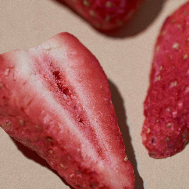 A close-up of three airy and textured halves of Bokksu White Strawberry 1 Piece on a beige surface. These delightful treats capture the essence of Nagano, Japan, making them perfect for any Bokksu Snack Box.