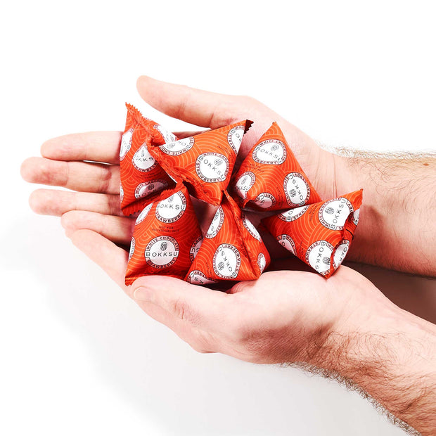 Hands holding several red, triangular snack packages with white and black labels, similar to a Bokksu White Strawberry 6-Piece Box from Bokksu featuring Japanese snacks.