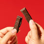 Two hands holding a snapped Nestle Japan Dark Chocolate Kit Kat bar against a red background. thumbnail 3