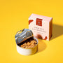 A tin of Bokksu Tinned Shirasu Anchovies with Cod Roe, partially open, is placed next to its packaging on a yellow background. The packaging is branded with &quot;Bokksu&quot; and highlights the fresh catch from Miyazaki Port. thumbnail 2