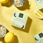 A package of Bokksu Tinned Shirasu Anchovies with Yuzu Pepper (2-Pack) beside bowls of anchovies and whole lemons on a yellow surface. thumbnail 3