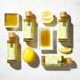 A trio of Bokksu Yuzu Hot Sauce bottles, two square dishes brimming with the spicy and tangy sauce, and two halved lemons sit on a light surface. thumbnail 5