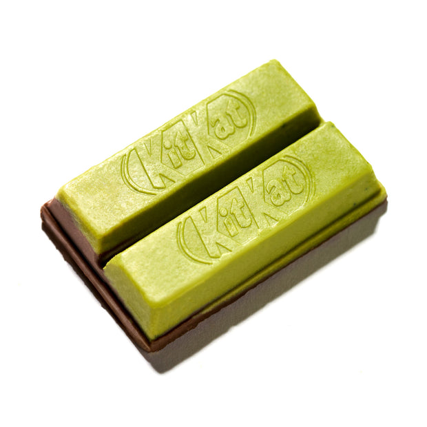 Two Japanese Kit Kats from Nestle Japan, featuring a brown chocolate base with green tea flavor and embossed logos, are displayed against a pristine white background as part of the Green Tea Double Layer (3-Pack).