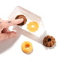 A hand with a small tattoo touches one of four different colored cereal pieces from a Kracie Popin Cookin DIY Candy: Donut kit on a white surface and container. thumbnail 4
