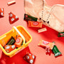 Assorted KitKat bars in orange, green, and red wrappers are spread on a red surface, accompanied by a cloth bag and a small yellow basket from the Bokksu Kawaii Gift Pack - Stationery Surprises &amp; Japanese Chocolate Treats. thumbnail 5