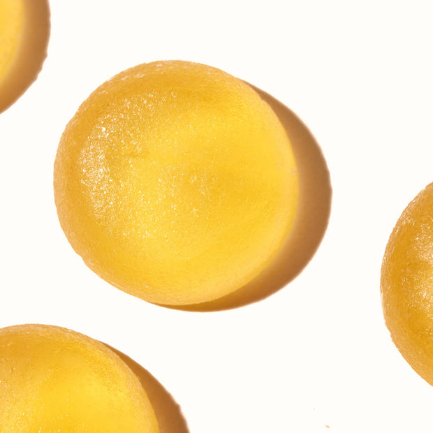 Close-up of three round, yellow, translucent objects arranged against a white background. They appear smooth and glossy with shadows visible, suggesting they are lit from above. These Kasugai Frutia Yuzu Gummy candies by Kasugai evoke the refreshing summery treat of Yuzu with their bright and inviting appearance.