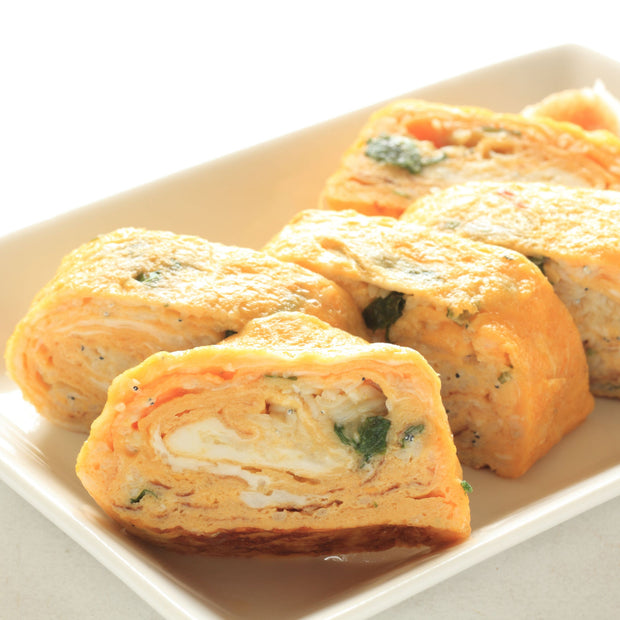 A plate of sliced rolled omelette with visible layers and herbs, infused with the umami-rich flavor of Bokksu Tinned Shirasu Anchovies Variety Pack (3-Pack) from Bokksu Market.